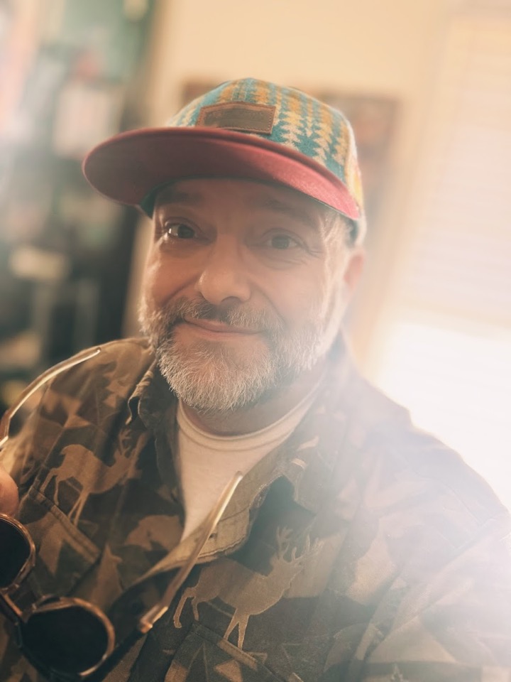 Portrait of Nathan Davis wearing a patterned cap and camouflage shirt.